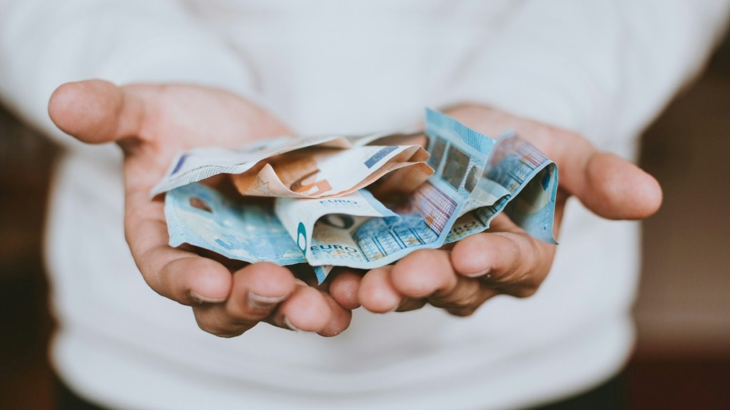 Osoba wyciągająca dłonie, na których leżą banknoty euro. Osoba wyciągająca dłonie, na których leżą banknoty euro.