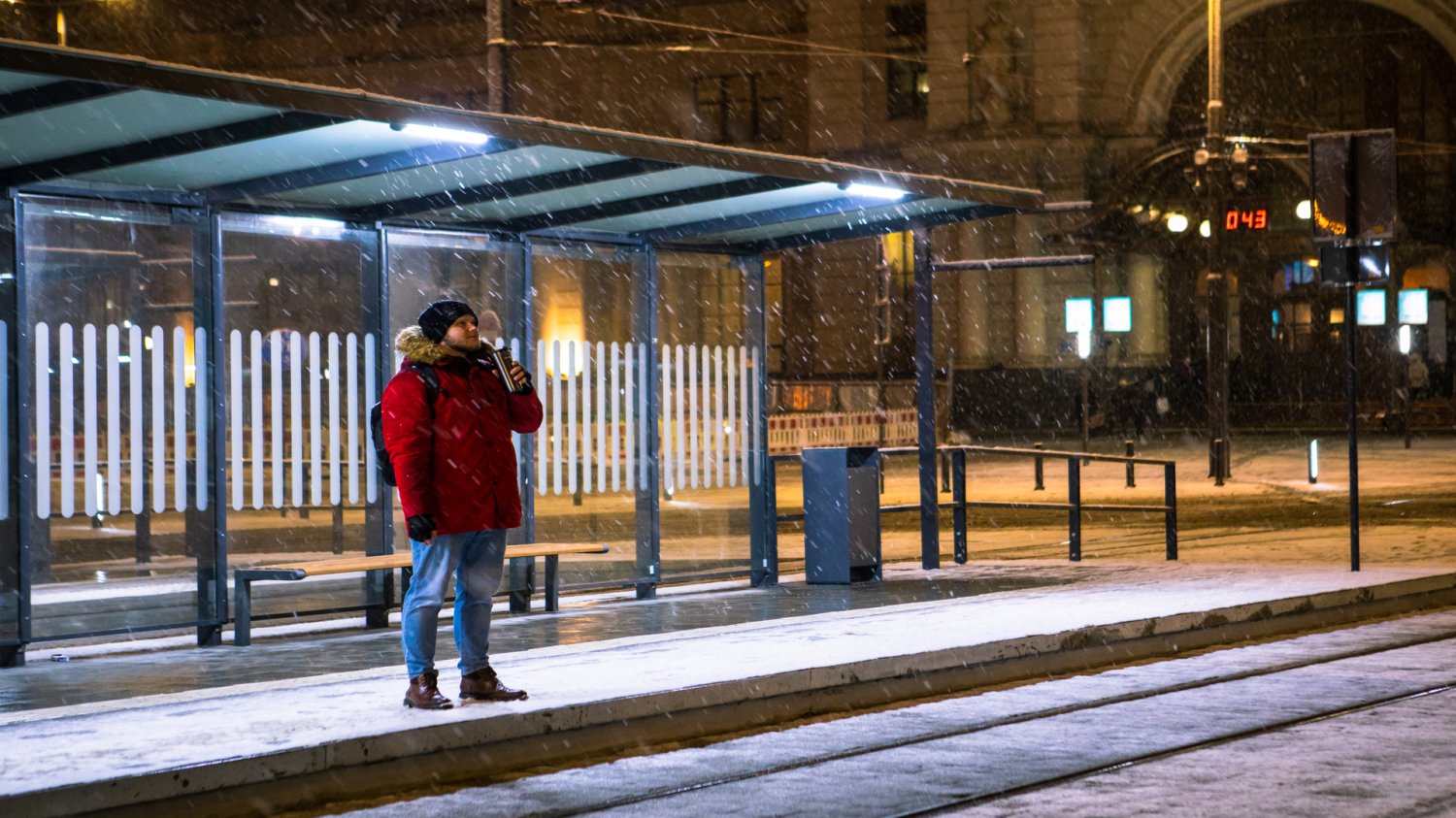 Nowy Tramwaj w Warszawie. Dworzec Zachodni jako główny punkt przesiadkowy. Mężczyzna w czerwonej kurtce na przystanku tramwajowym. Wieczór, pada śnieg.