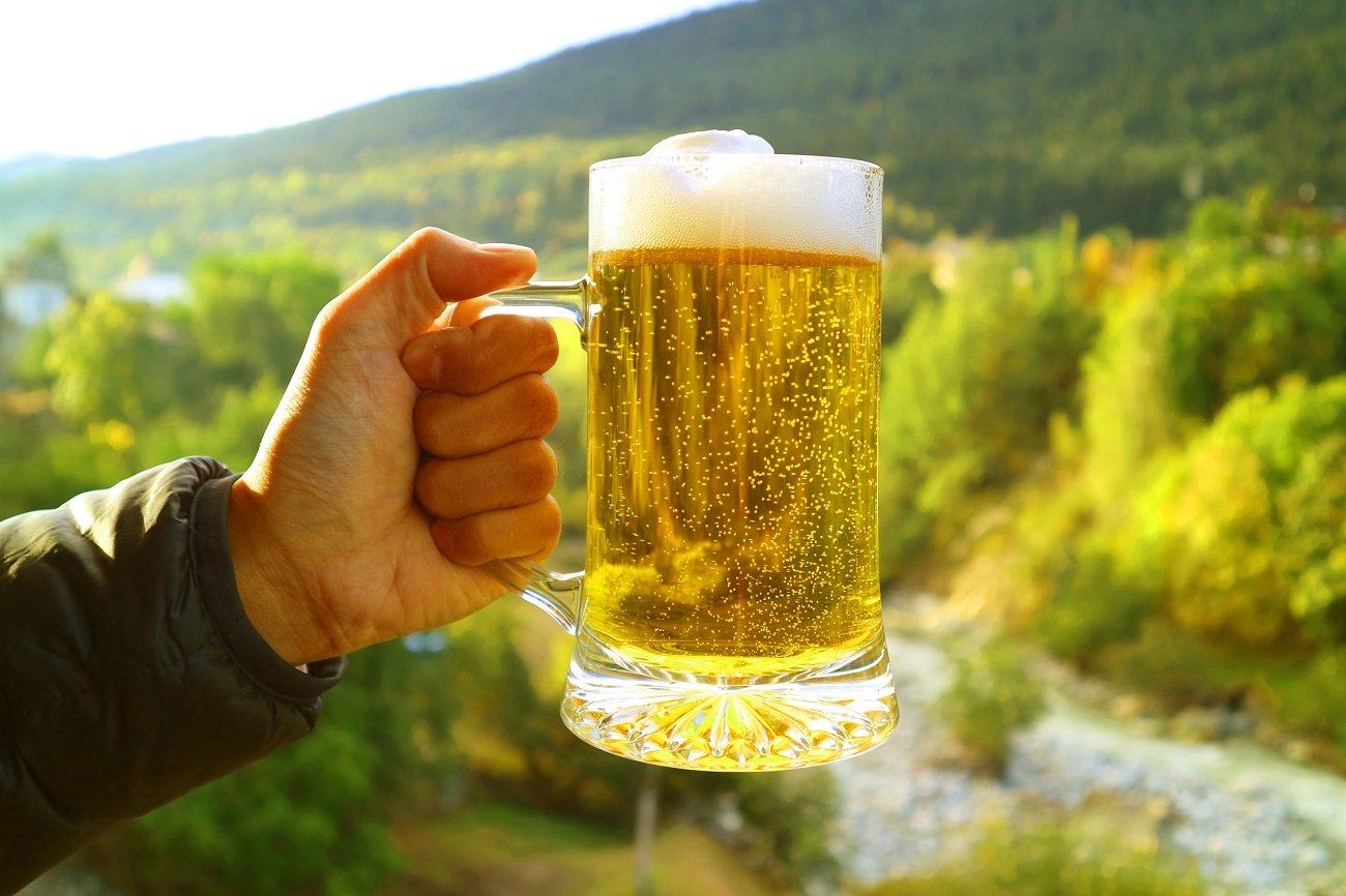 Mężczyzna trzyma piwo na tle rzeki.