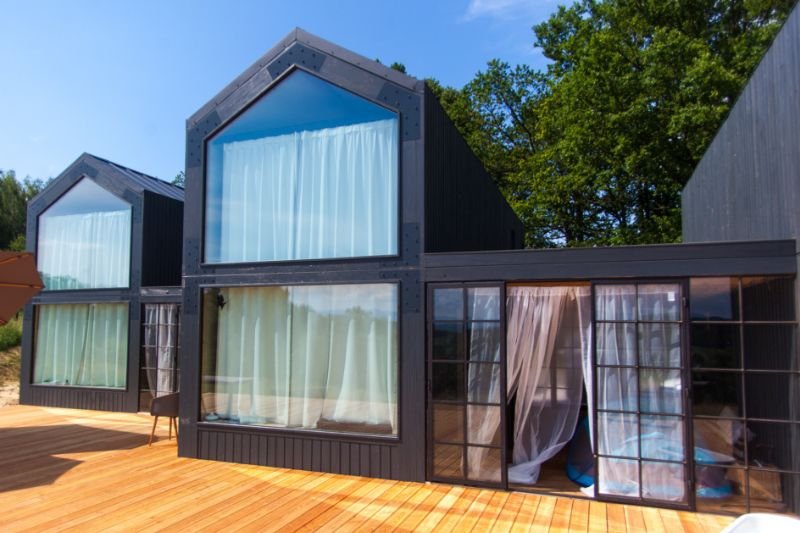 Mikrodomy firmy Magbos z dużymi oknami i przeszklonym tarasem, w tle niebieskie niebo i zielone drzewa