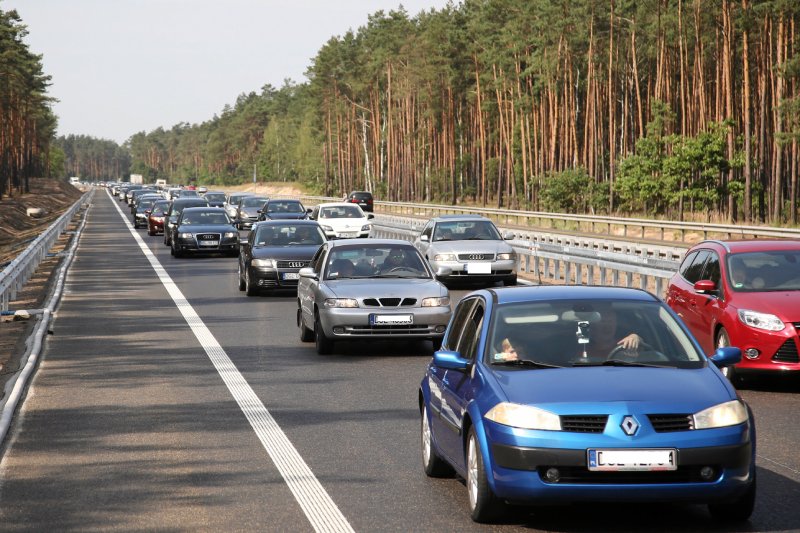 Samochody osobowe stojące w korku na drodze ekspresowej, która biegnie przez las.