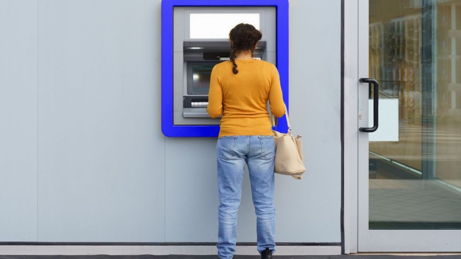 kobieta w  żółtej bluzce stoi przed bankomatem