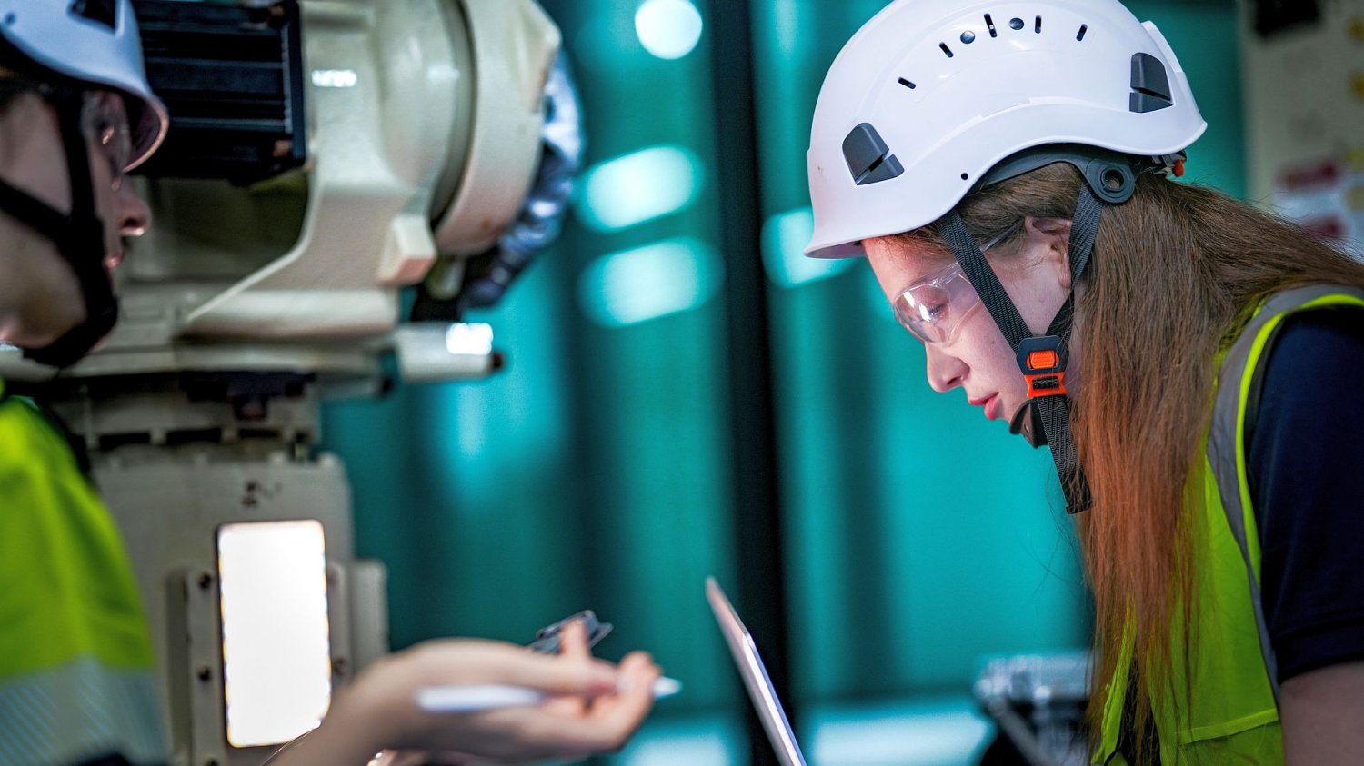 dwie kobiety inżynierki w kaskach i kamizelkach bezpieczeństwa pracują z ramieniem robota