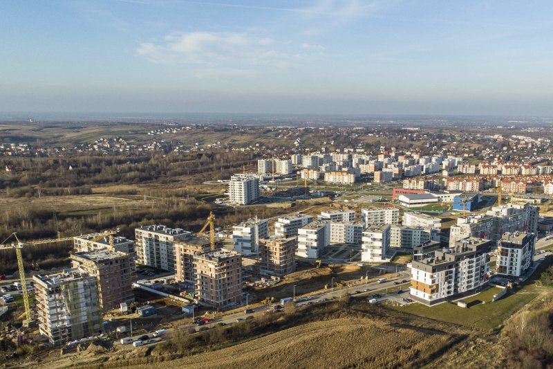 Widok panoramiczny na osiedle mieszkaniowe w Rzeszowie. Na pierwszym planie znajduje się nowe osiedle: część bloków mieszkalnych jest już gotowa, część jest jeszcze w budowie, ustawione przy nich są żurawie.