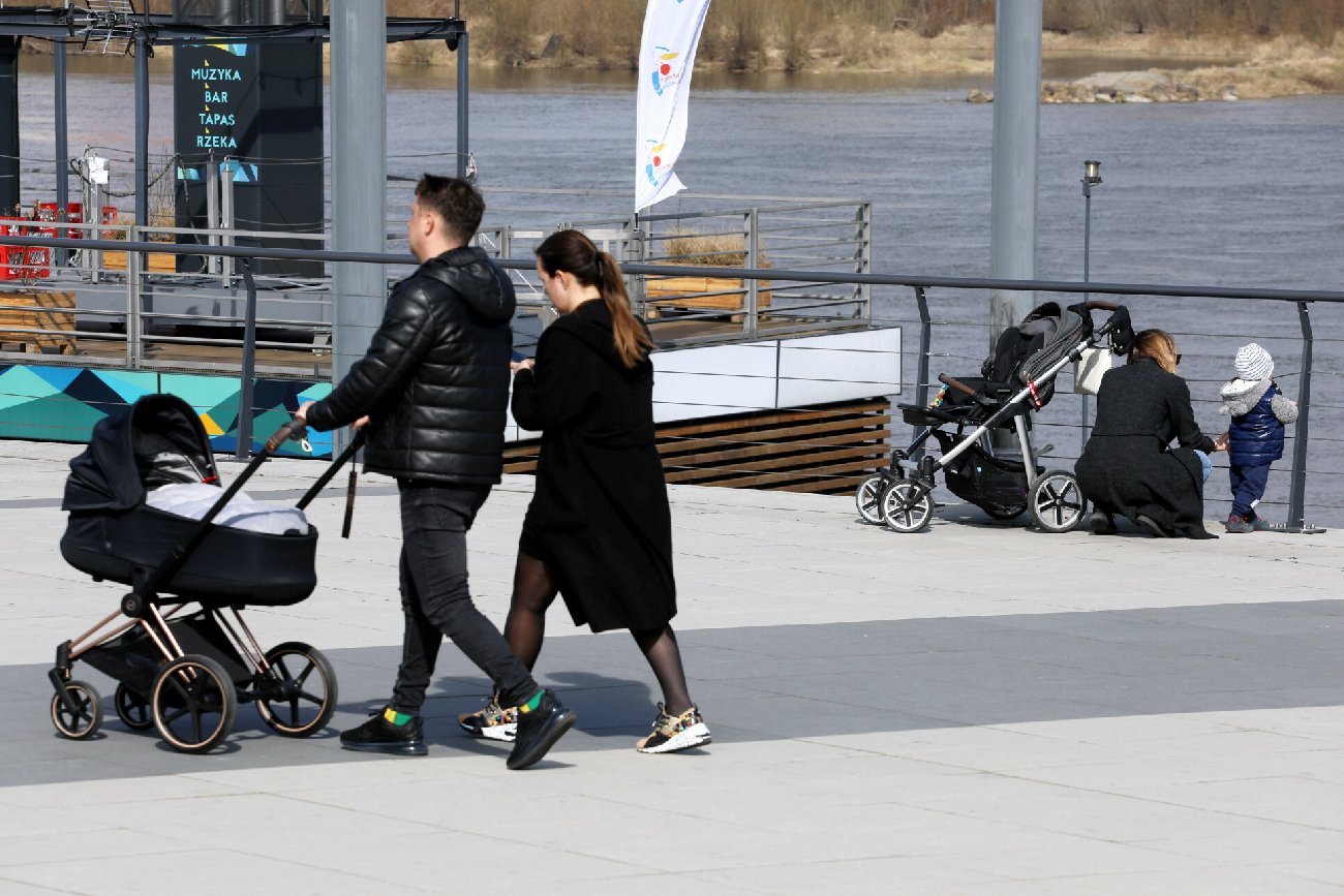 młodzi rodzice w czarnych strojach na spacerze z wózkiem i małymi dziećmi na bulwarach na Wisłą w Warszawie
