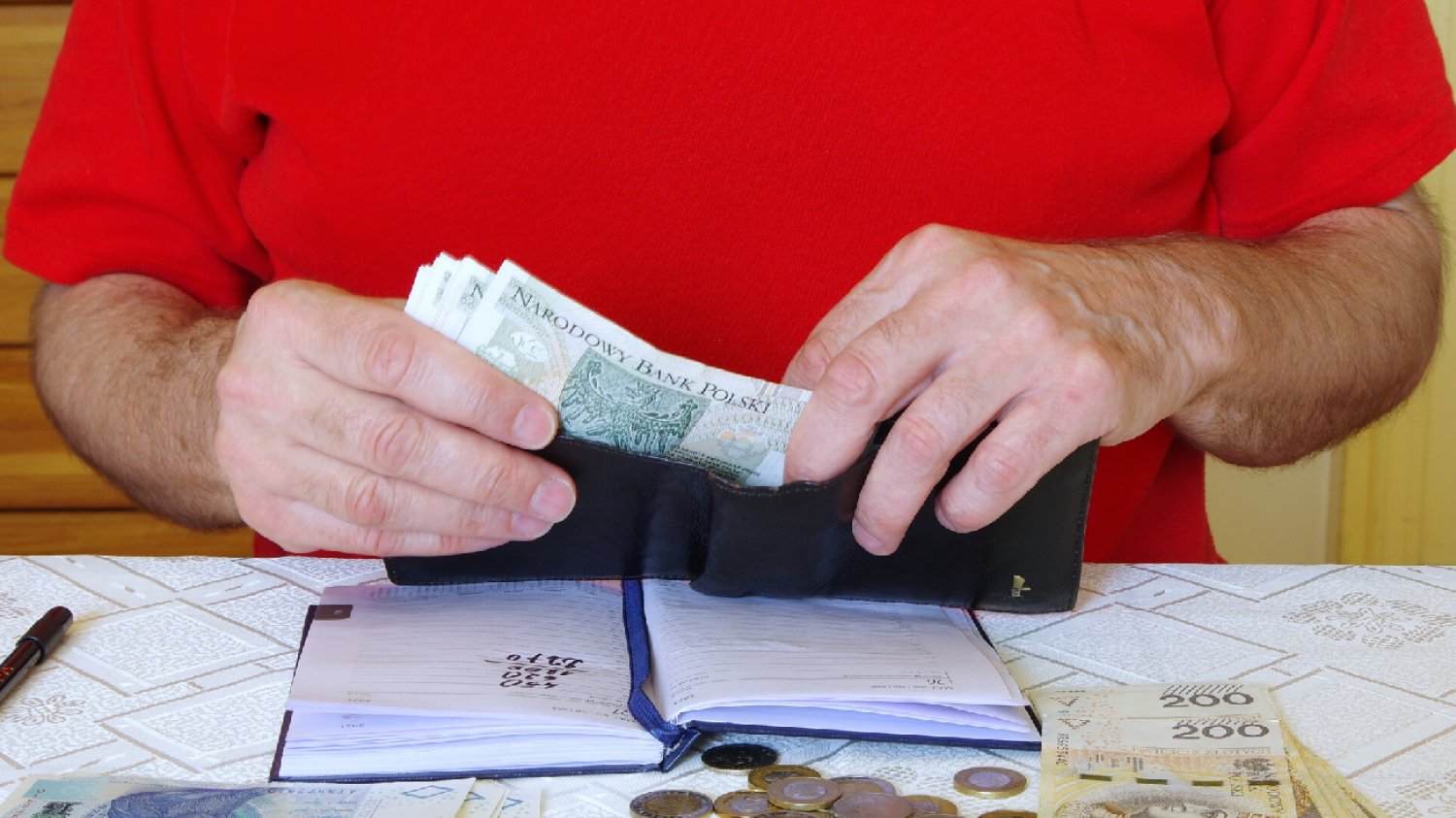 mężczyzna w czerwonej koszulce oblicza domowy budżet, miesięczne koszty utrzymania, polskie pieniądze, banknoty i monety
