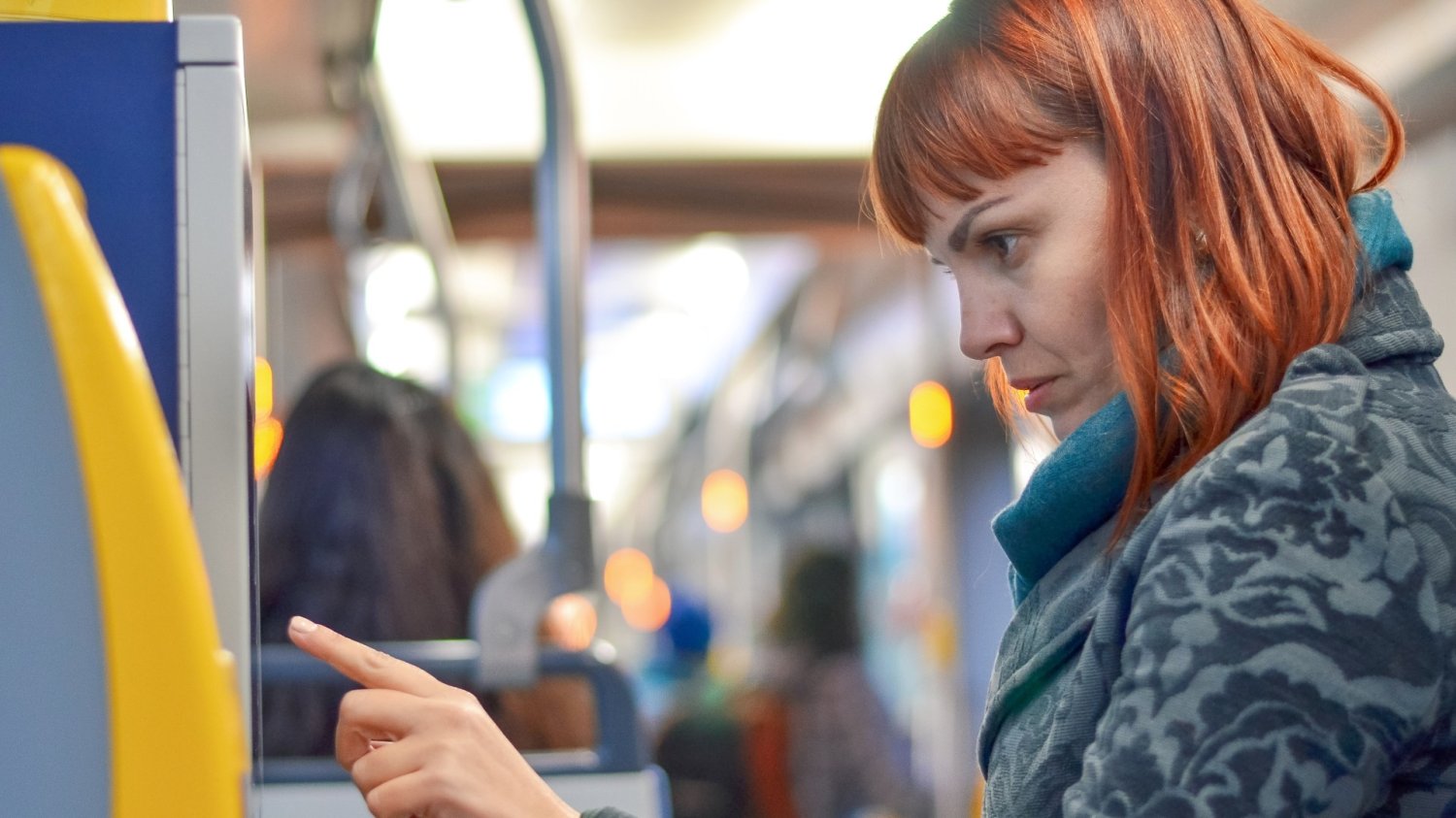 Kobieta w autobusie naciska przycisk automatu do zakupu biletów.