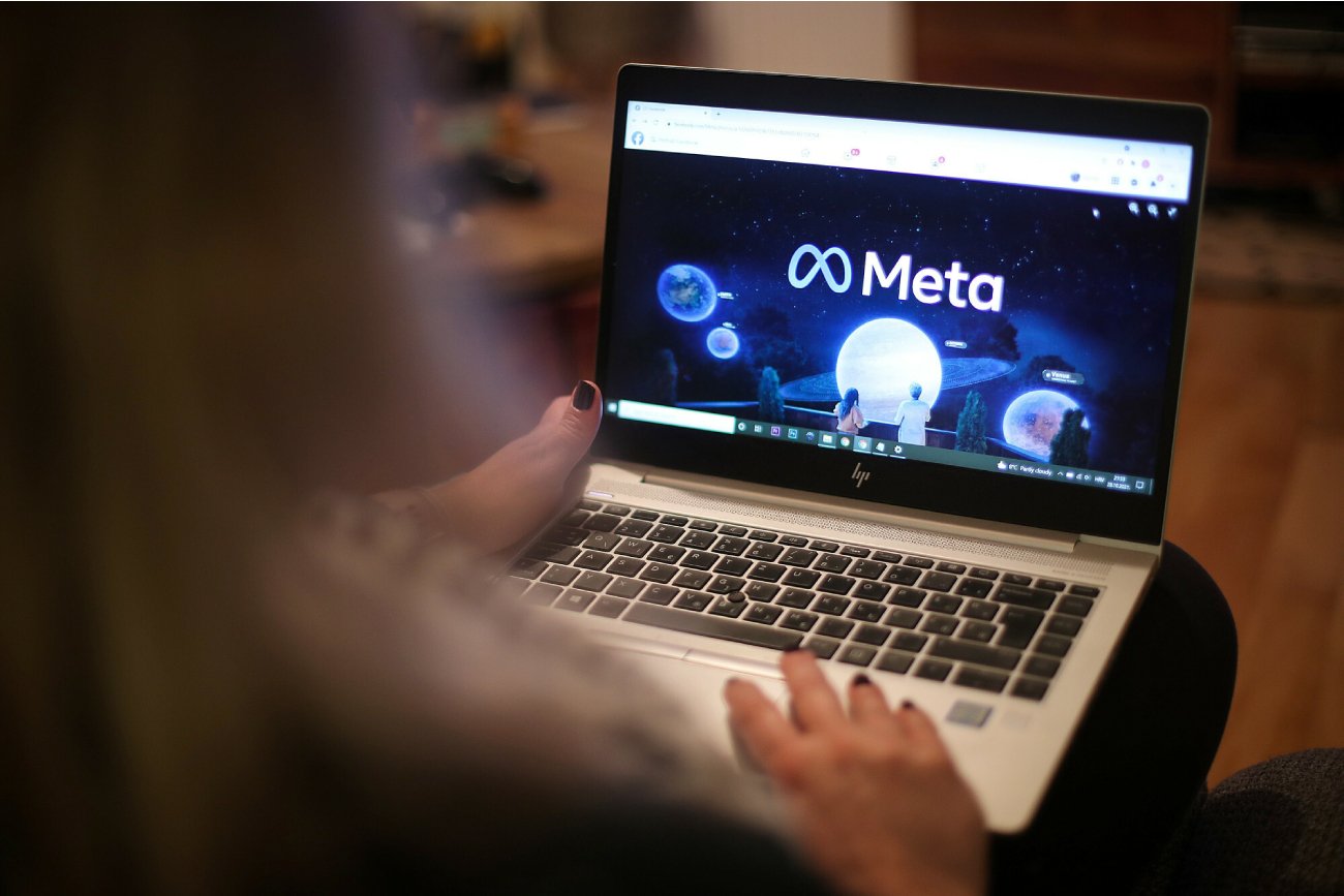 kobieta patrzy na laptop z otworzoną kartą Facebook Meta i kilka w ikony na monitorze przenośnego komputera