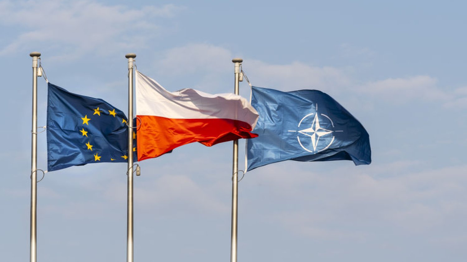 Flagi Unii Europejskiej, Polski i NATO powiewające na wietrze.