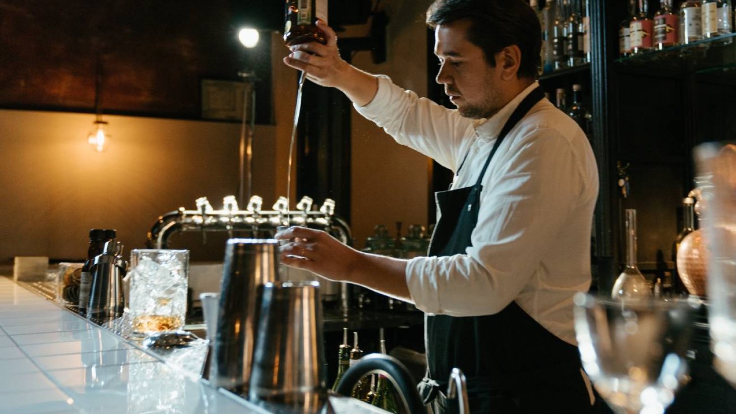 Samotny barman za barem lokalu gastronomicznego. Mężczyzna nalewa drinka.