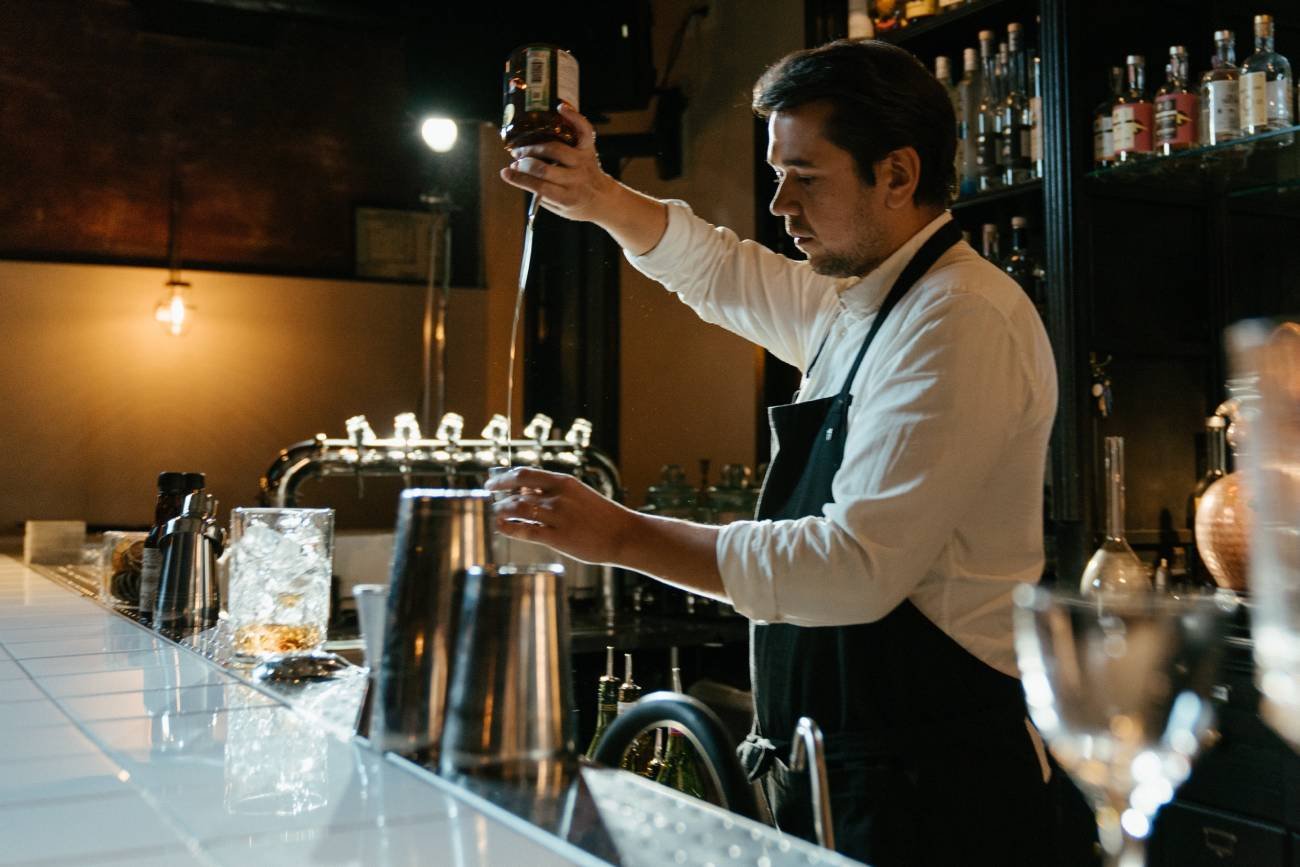 Samotny barman za barem lokalu gastronomicznego. Mężczyzna nalewa drinka.