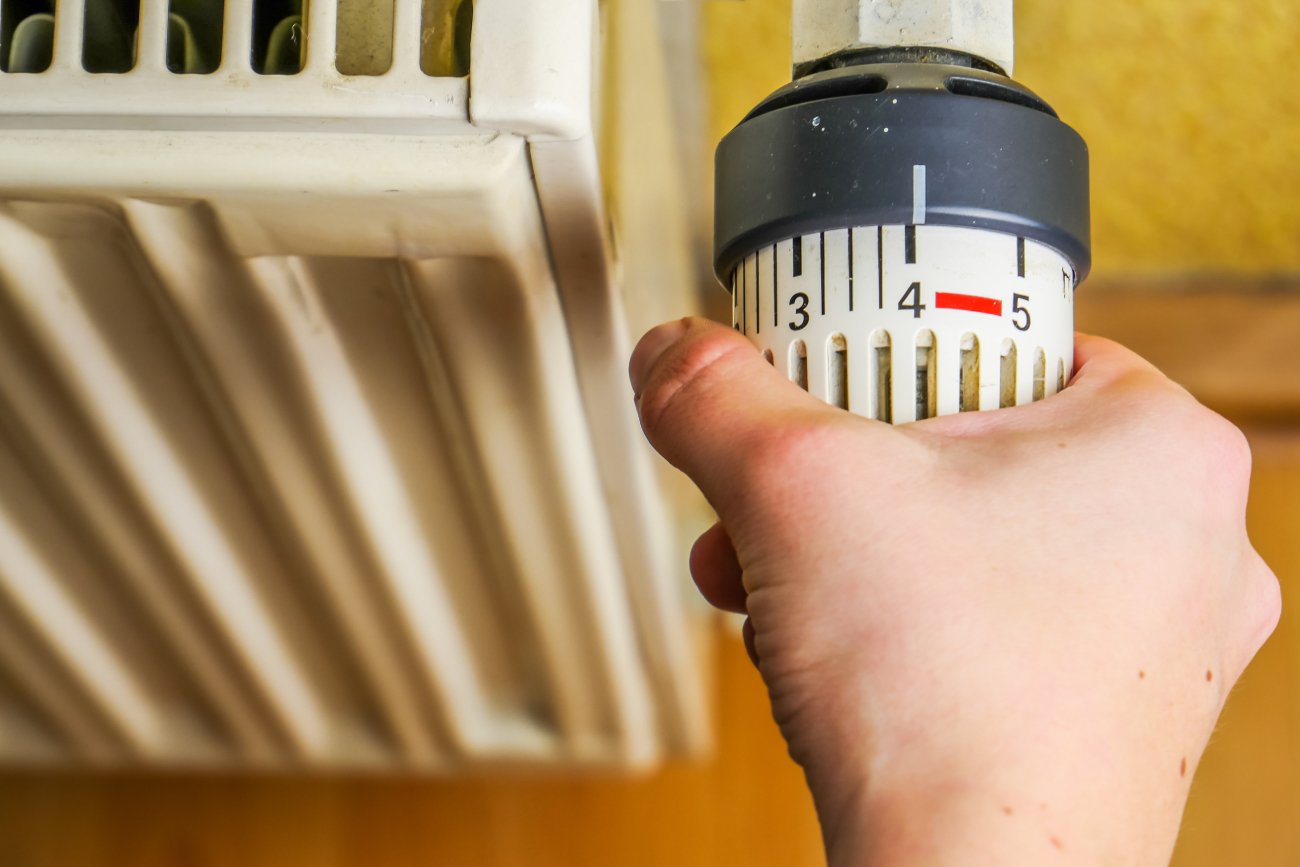 dłoń mężczyzny odkręca termostat grzejnika na maksymalną temperaturę