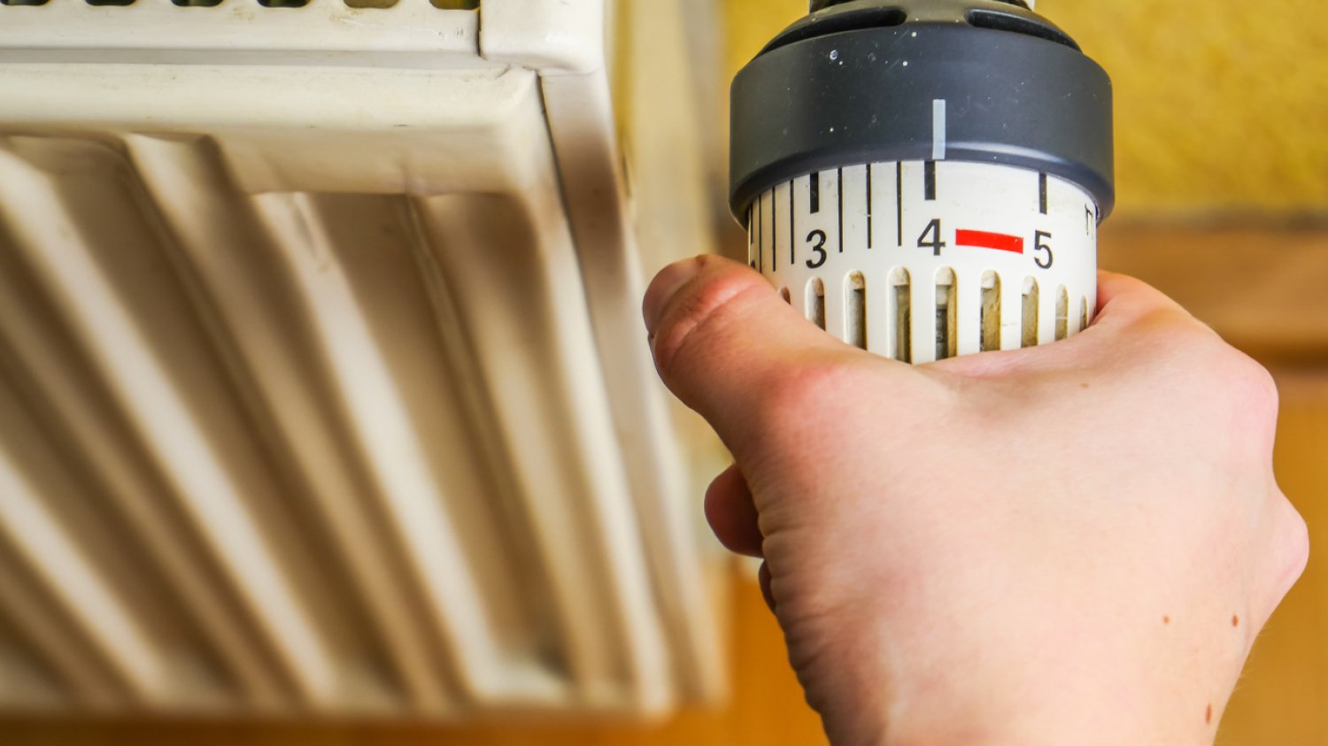 dłoń mężczyzny odkręca termostat grzejnika na maksymalną temperaturę