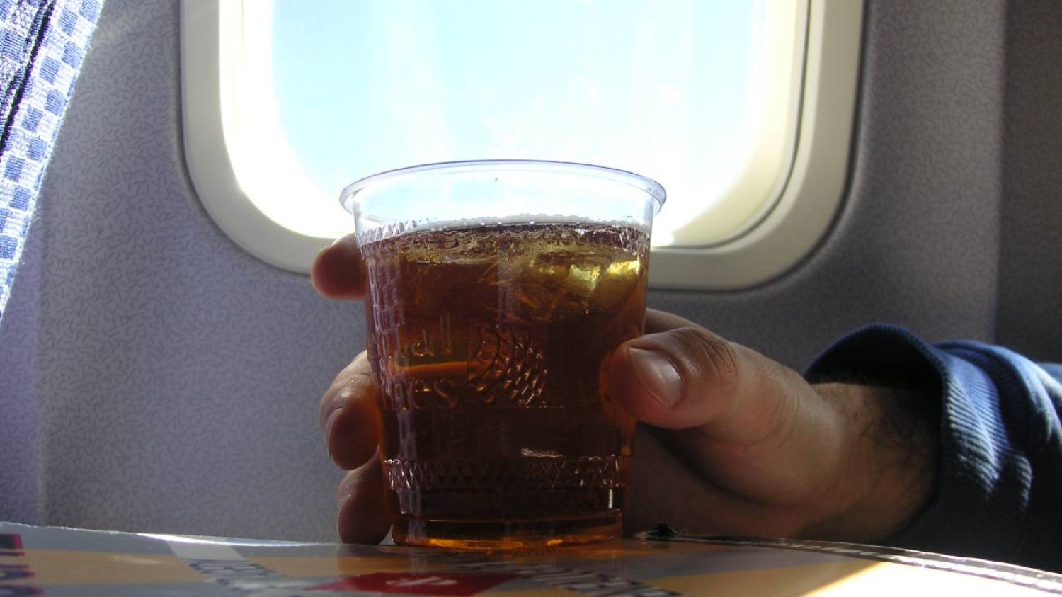 Wnętrze samolotu, ręka trzymająca napój - Jack Daniel's z colą.