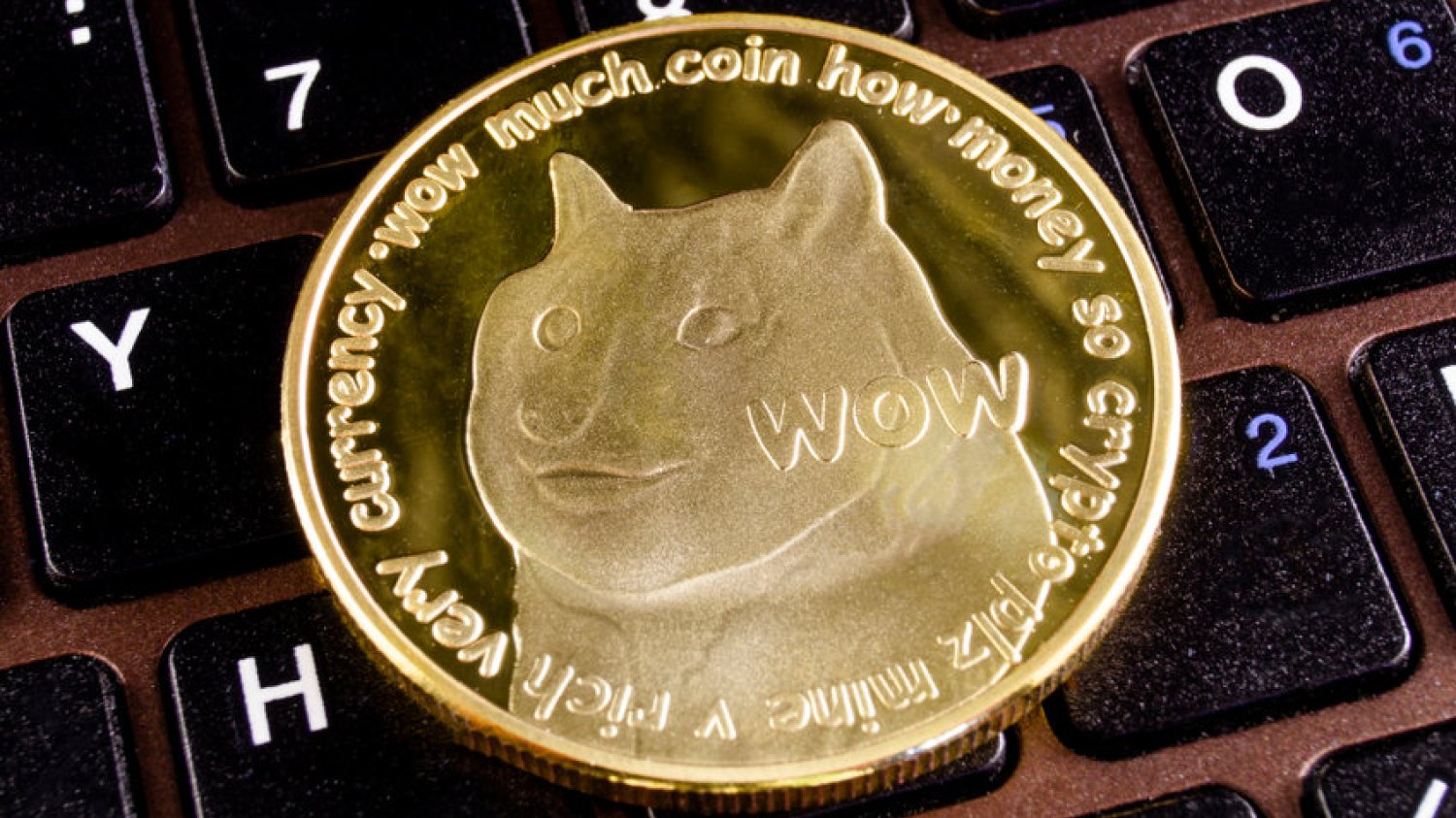 Dogecoin w formie fizycznej monety leżący na klawiaturze laptopa