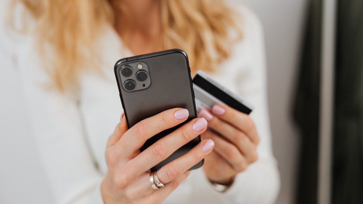 Kobieta trzymająca w ręku kartę płatniczą i telefon.