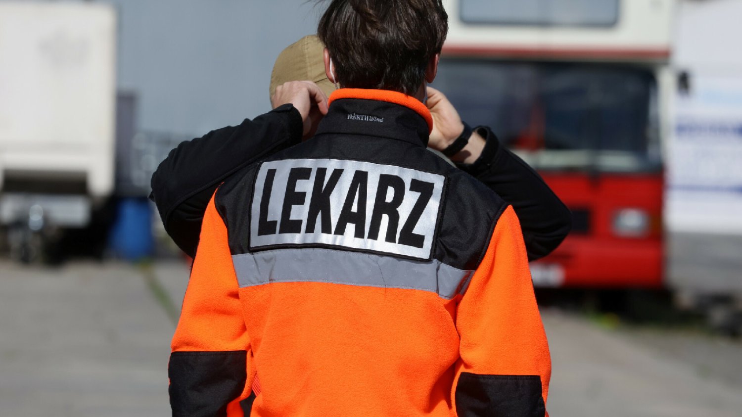 zawodowy lekarz w pomarańczowym uniformie rozmawia z mężczyzną odwrócony tyłem do obiektywu