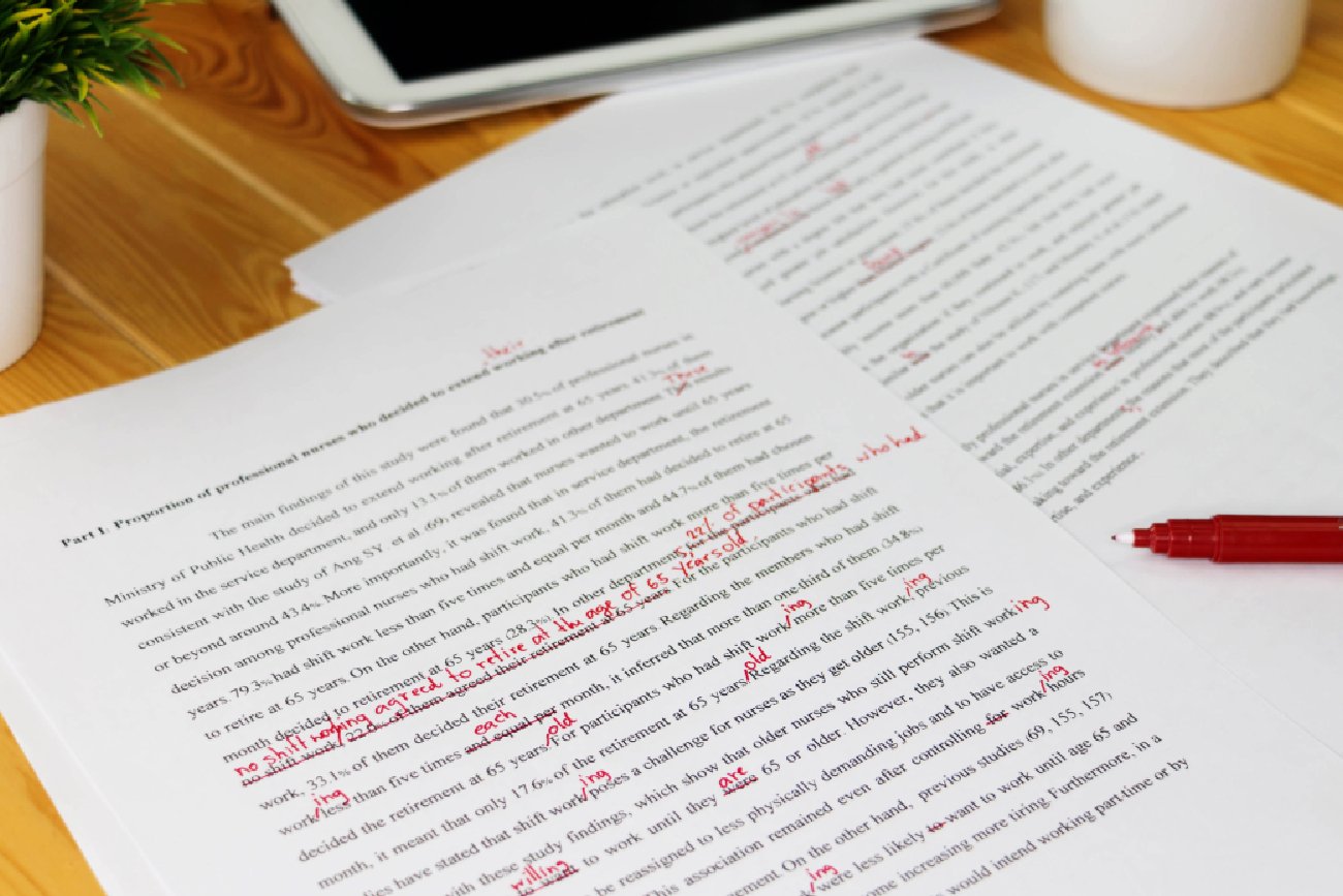 czerwony cienkopis robi poprawki na wydrukowanym dokumencie, który leży na drewnianym biurku