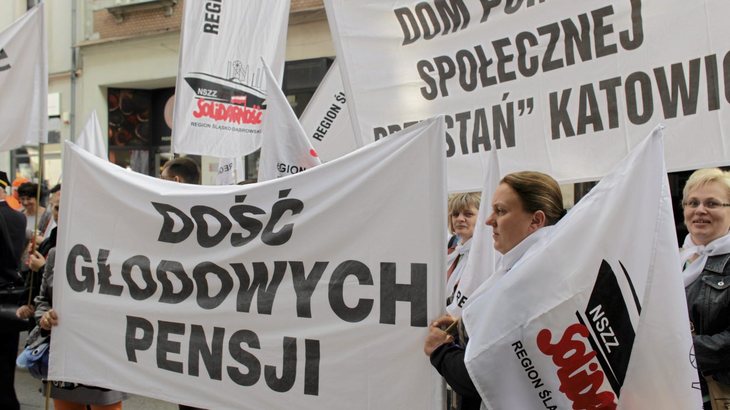 Ludzie trzymają transparenty i protestują. Na jednym transparencie napis "Dość głodowych pensji".