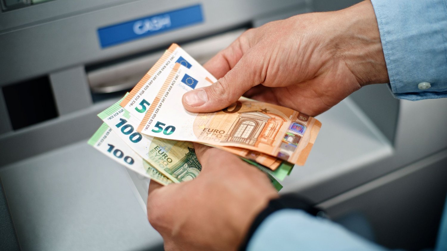 banknoty euro w ręku mężczyzny na tle bankomatu
