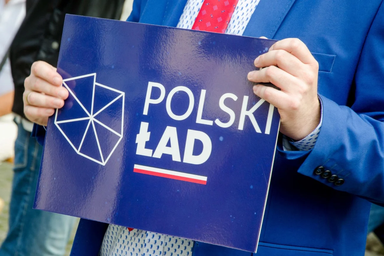 mężczyzna trzymający w dłoniach planszę "Polski Ład"
