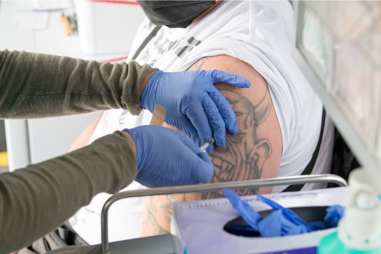 pielęgniarka w niebieskich rękawiczkach robi zastrzyk szczepionki na COVIS-19 pacjentowi z tatuażem na ramieniu