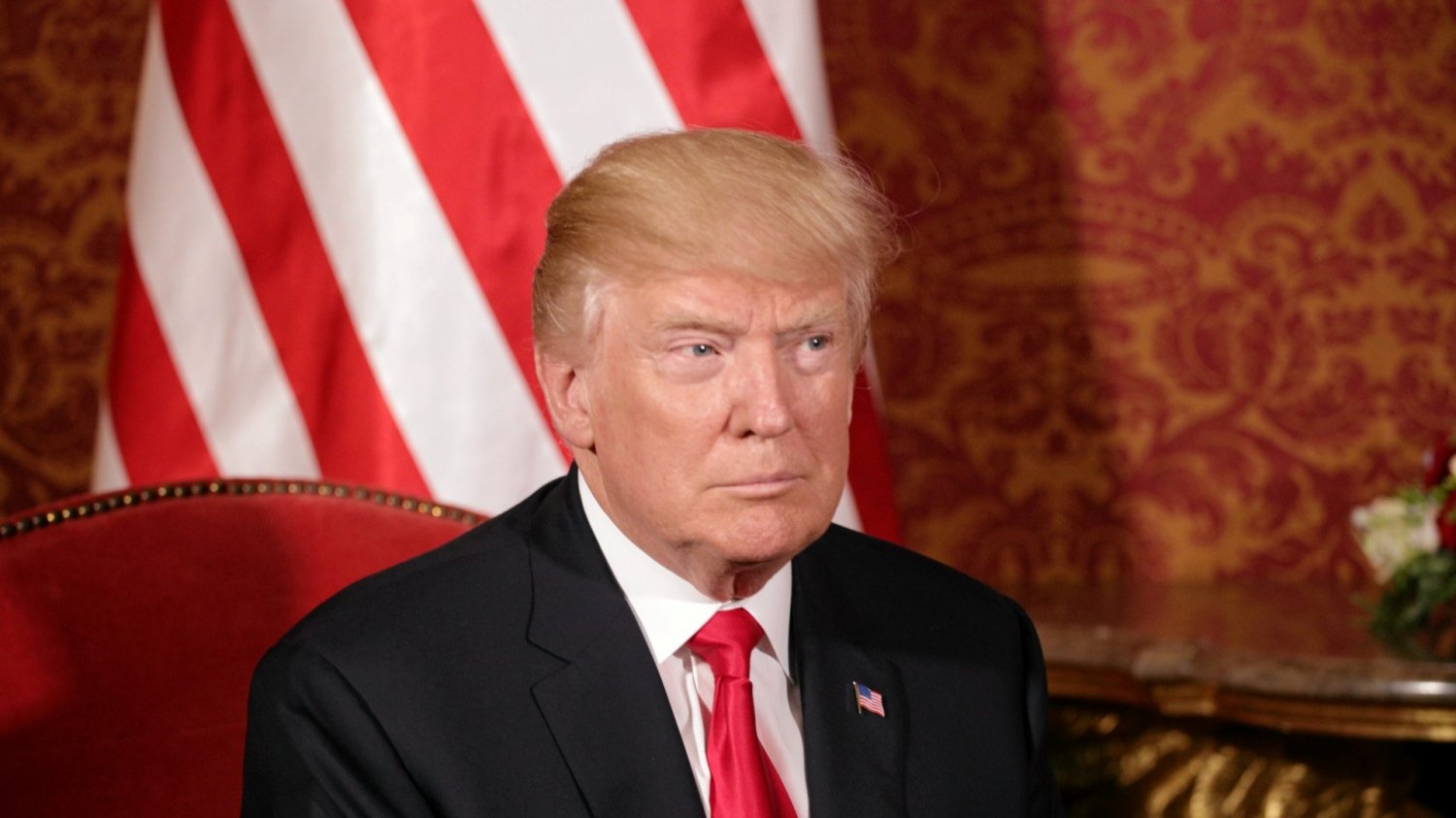 Prezydent USA Donald Trump z wizytą w Zamku Królewskim w Warszawie (2017). Donald Trump siedzący na ozdobnym krześle wewnątrz Zamku Królewskiego. Pod jego przywództwem USA prowadzą wojnę handlową z Chinami.