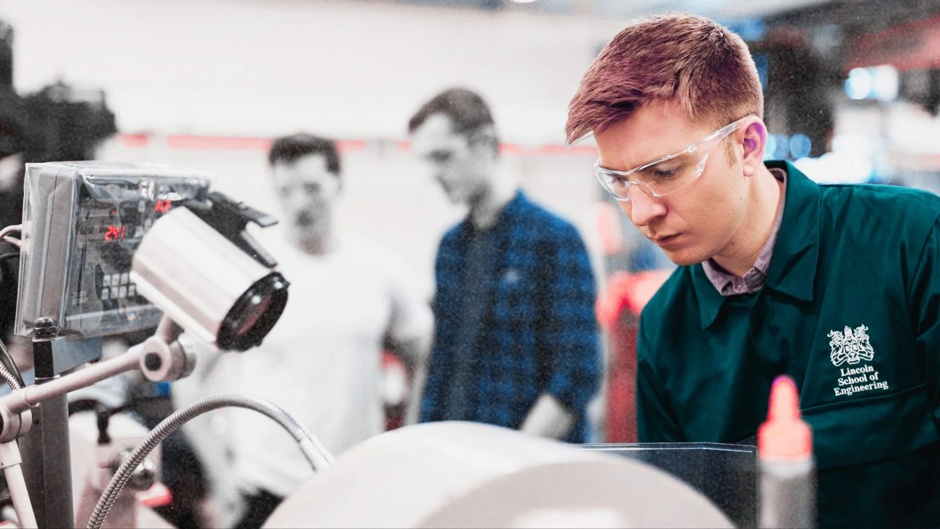 Młody mężczyzn pochyla się nad urządzeniem. Studenci szkoły inżynierii.