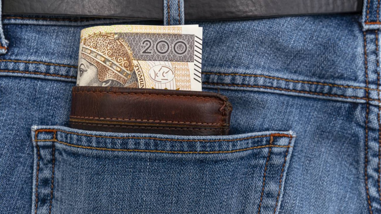 Banknot 200 zł wystaje z brązowego portfela. Portfel w tylnej kieszeni niebieskich jeansów.