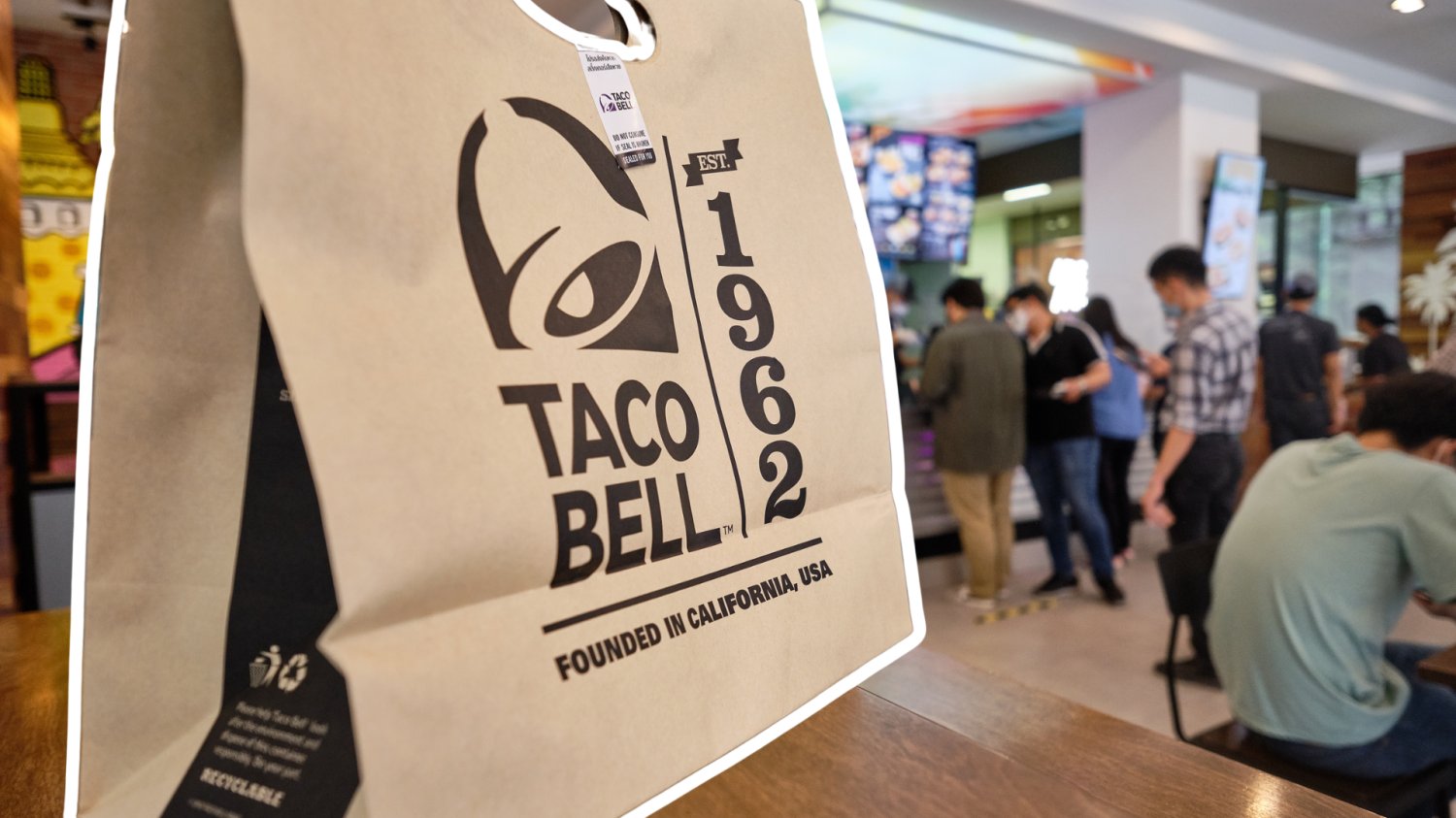 Fast-foodowy gigant wjeżdża do Polski. Meksykańska fala zaleje rynek gastronomii Torba z zamówieniem TACO BELL. W tle restauracja i klienci.