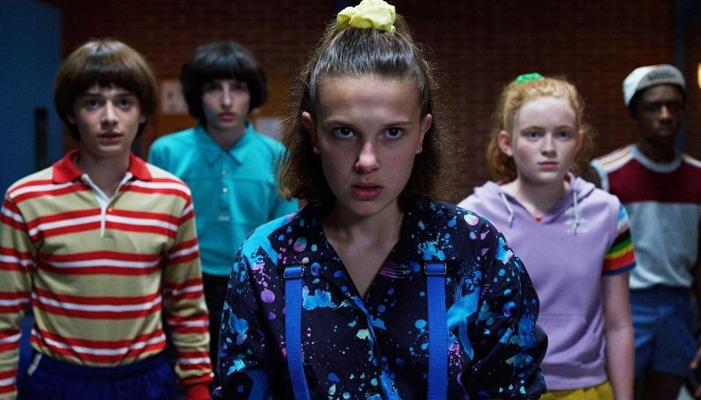 Postacie z serialu "Stranger Things". Na przodzie stoi Eleven z poważną miną