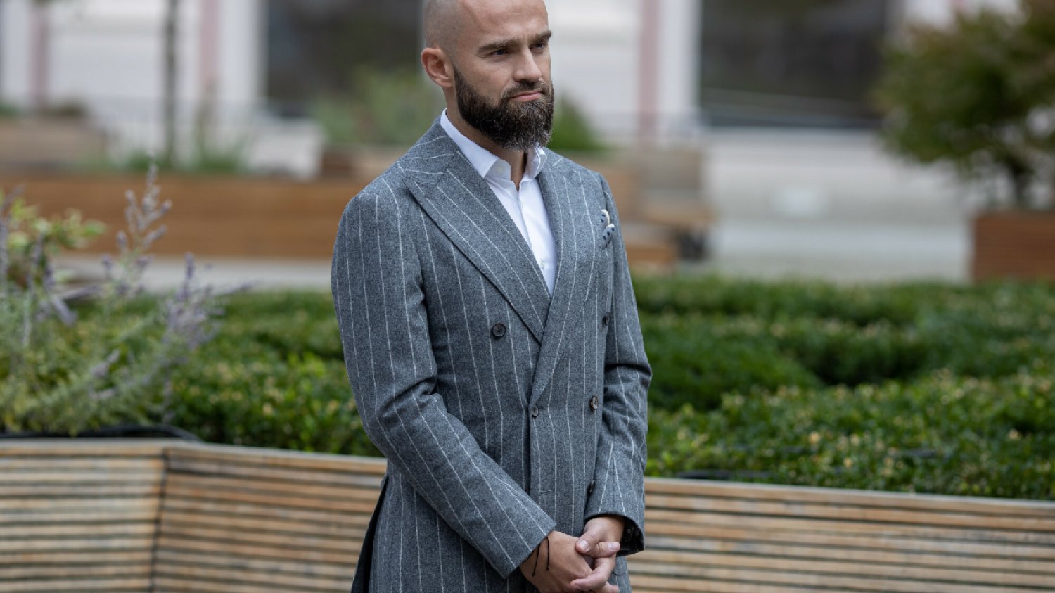 miliarder Sebastian Kluczyk w szarym garniturze stoi na tle zieleni podczas konferencji prasowej