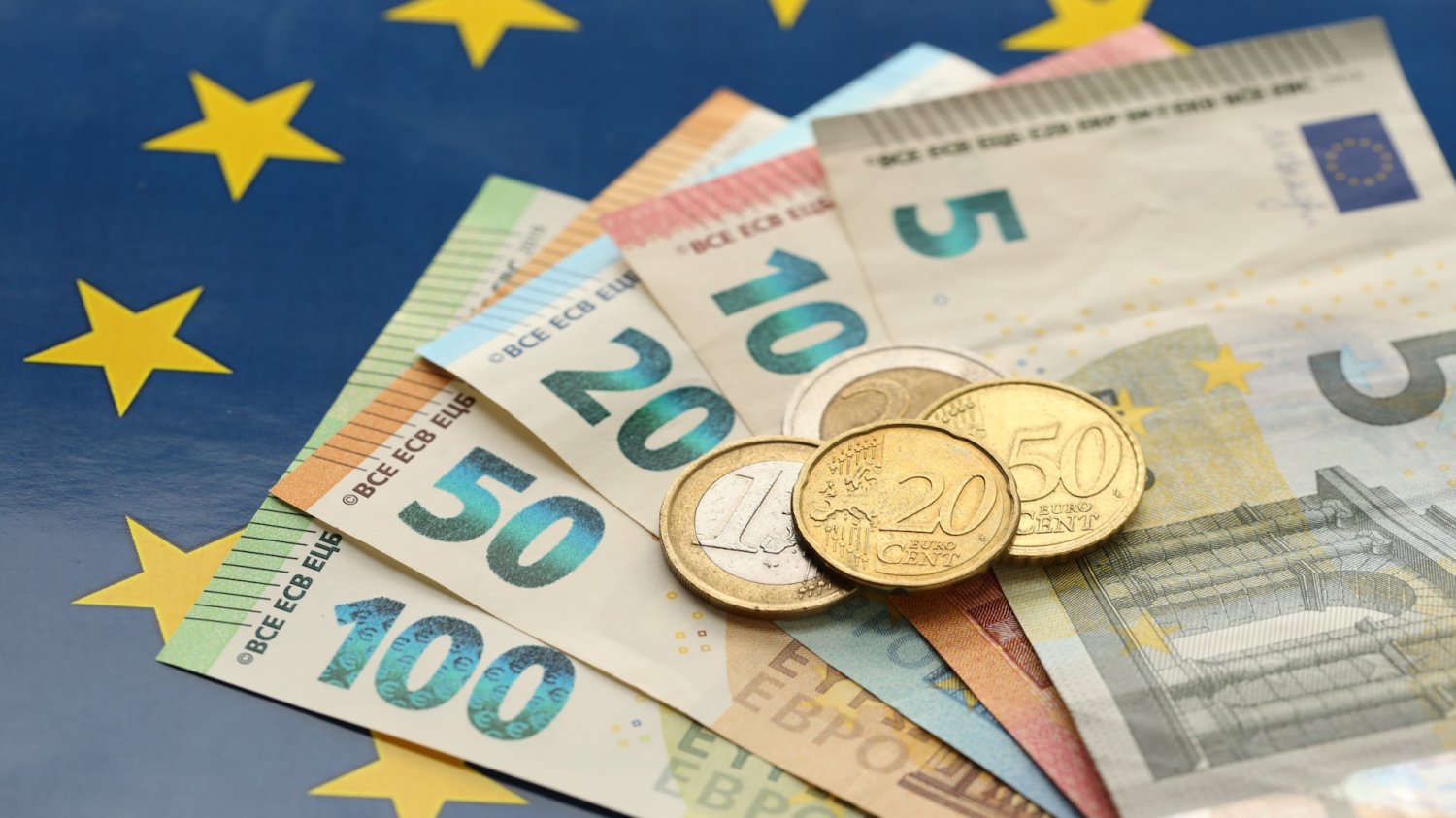 Banknoty i monety euro na tle flagi Unii Europejskiej. Polska sprzedała obligacje za 3 mld euro. Inwestorom nadal mało