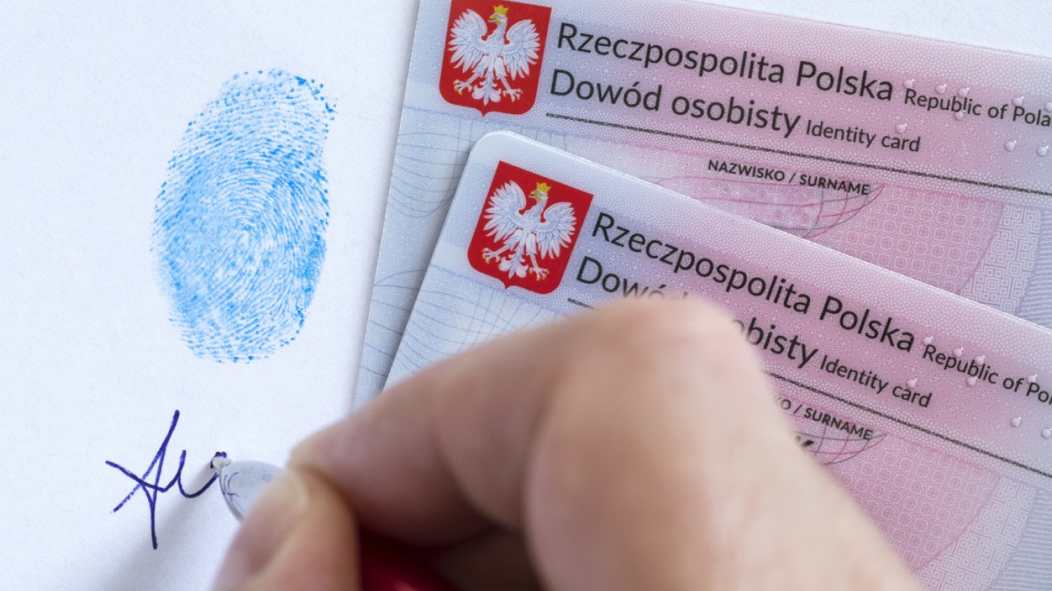 dłoń robi podpis pod odciskiem palca i w pobliżu dwóch polskich dowodów osobistych