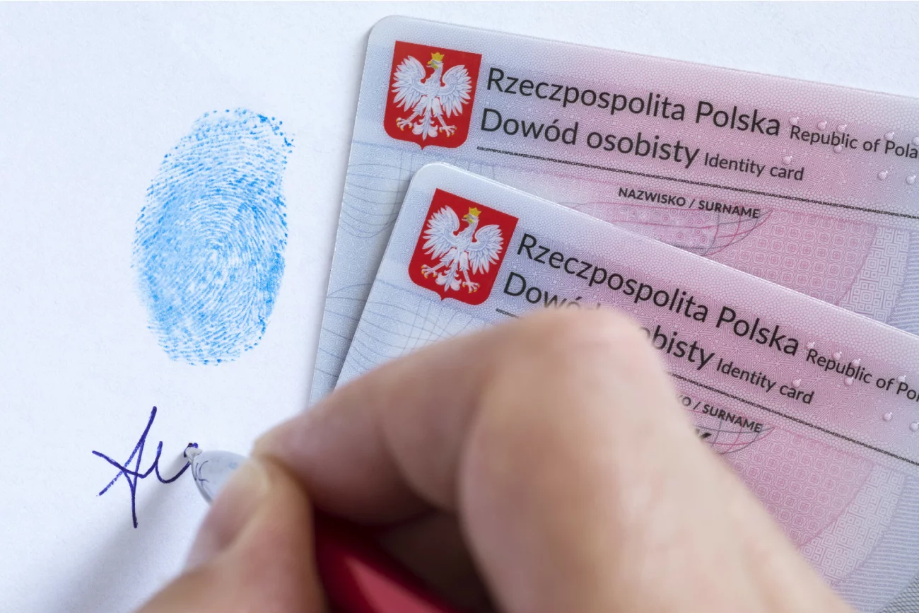 dłoń robi podpis pod odciskiem palca i w pobliżu dwóch polskich dowodów osobistych