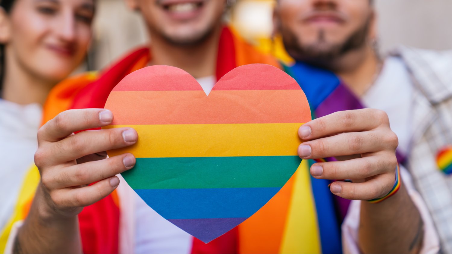 Państwo uznało małżeństwo, ale fiskus odmówił ulgi. Mamy w Polsce nowy paradoks Serce w barwach flagi LGBT. W tle osoby trzymające te flage.