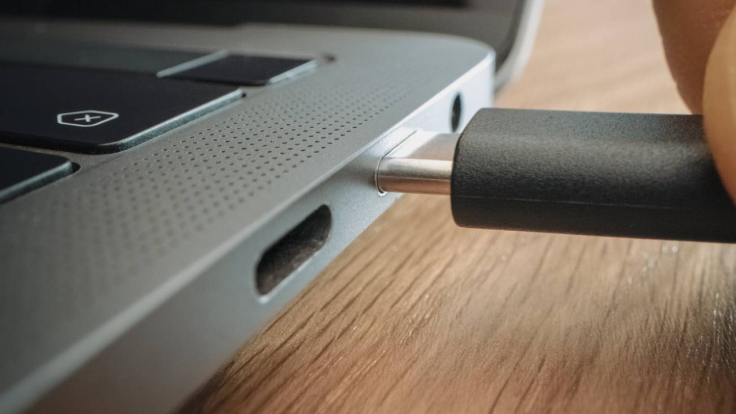 Ręka wkłada wtyczkę USB C do laptopa.