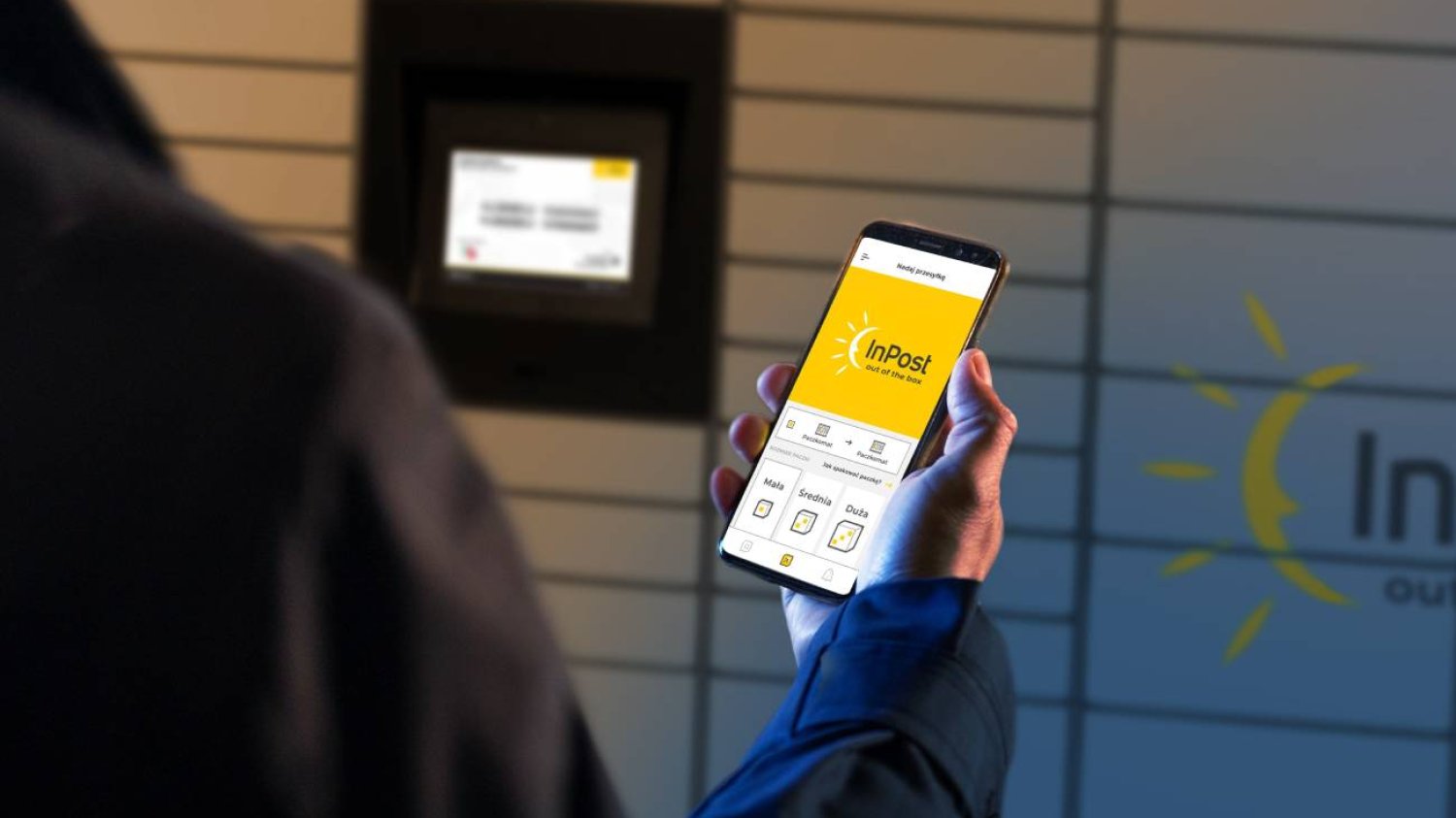 Mężczyzna używający aplikacji InPost, przed automatem paczkowym, tzw. paczkomatem.