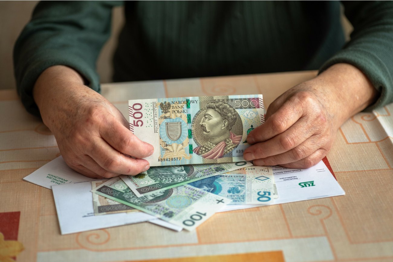 mężczyzna w zielonym swetrze trzyma w ręku banknot 500 złotych