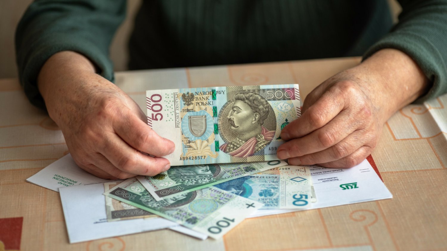 mężczyzna w zielonym swetrze trzyma w ręku banknot 500 złotych