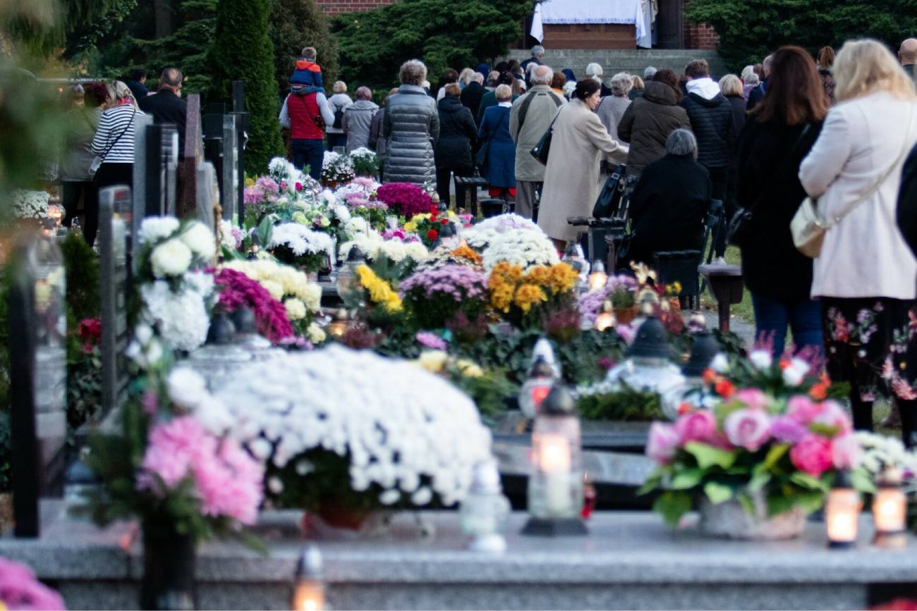 Ludzie zgromadzeni przy grobach na cmentarzu na Wszystkich Świętych.