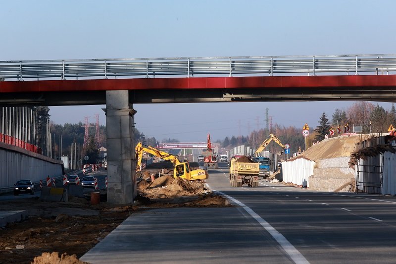 Budowa drogi pod wiaduktem. Koparka i inne maszyny budowlane w tle.