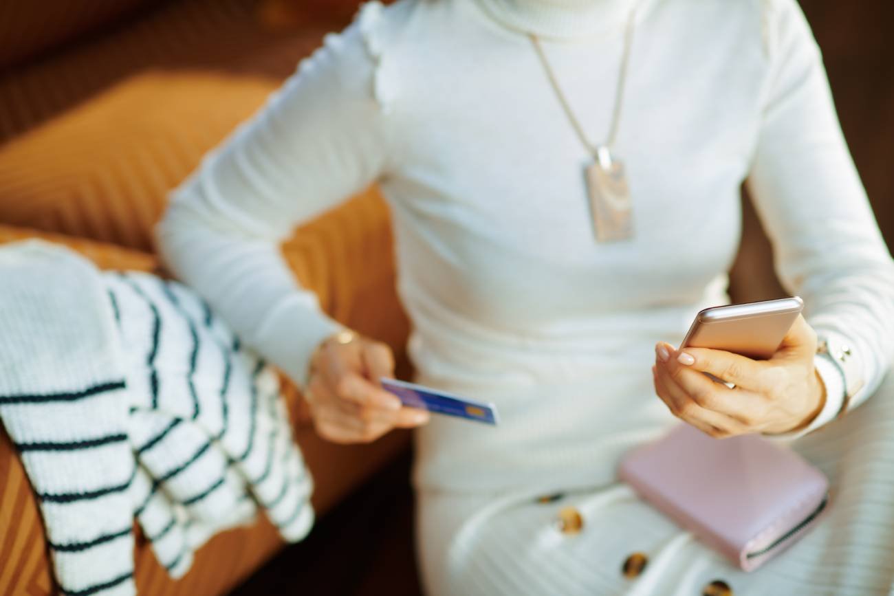 Kobieta siedząca z telefonem i kartą płatniczą w ręce