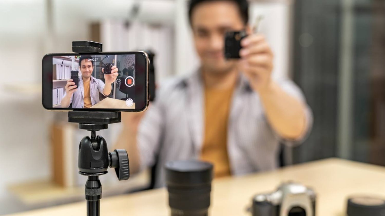 Youtuber nagrywa komórką filmik o aparacie fotograficznym. Focus na smartfona na statywie.