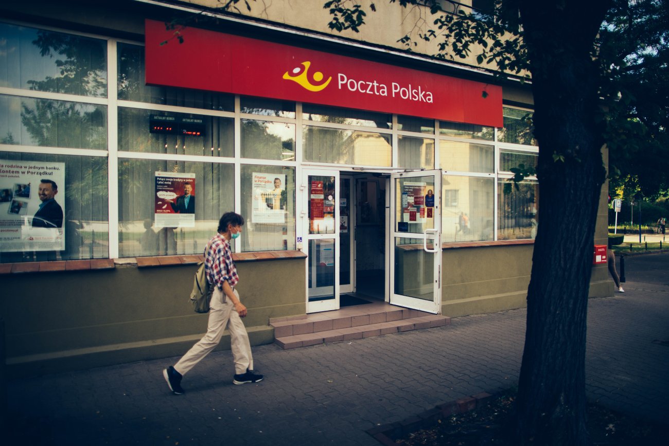 Mężczyzna w letnim ubraniu przechodzący koło otwartej placówki Poczty Polskiej.