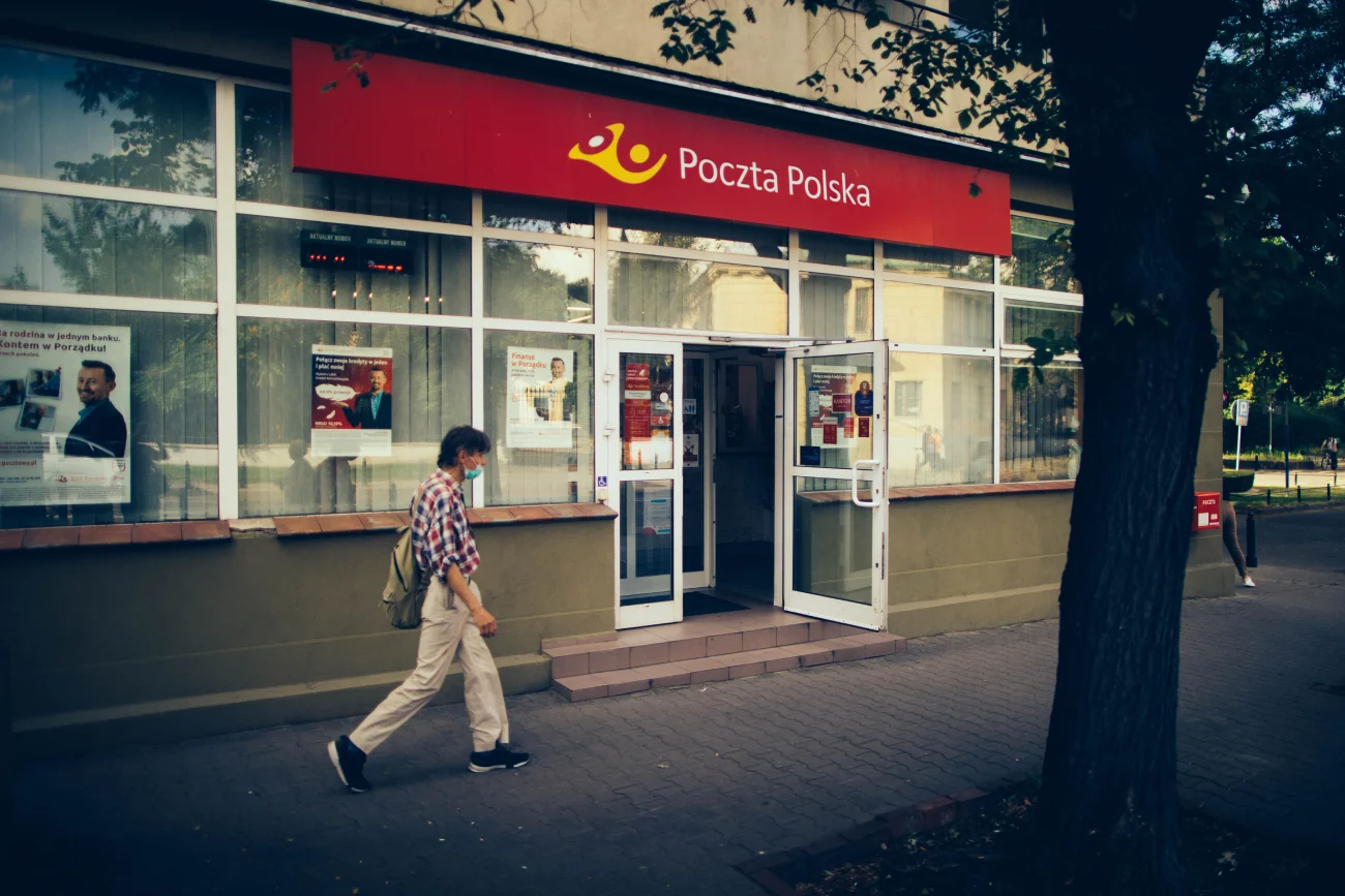 Mężczyzna w letnim ubraniu przechodzący koło otwartej placówki Poczty Polskiej.