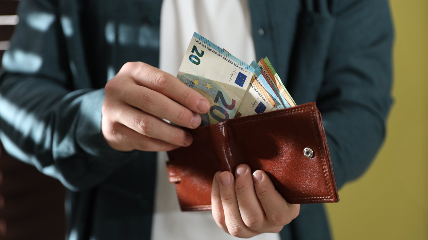 Osoba trzyma portfel w rękach i przelicza banknoty.