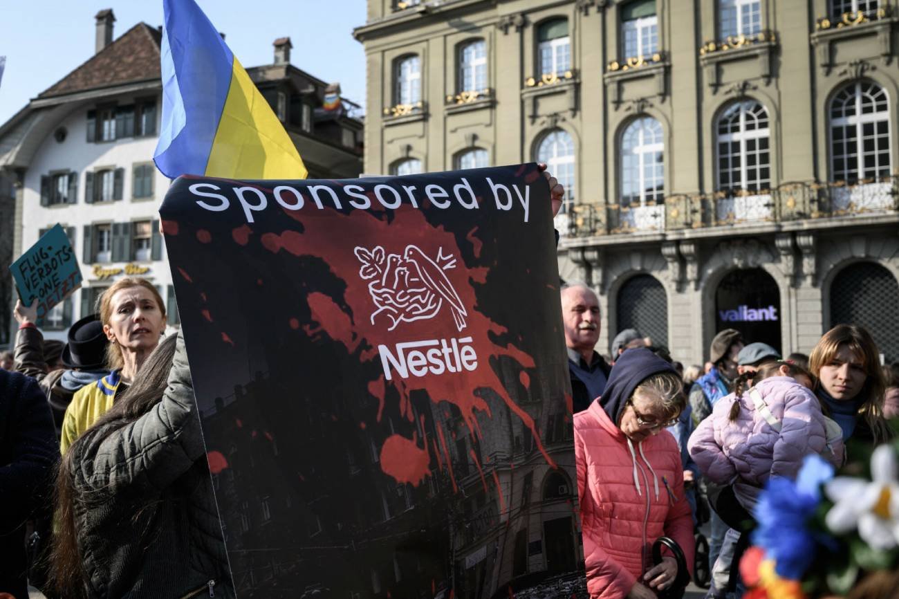 Protestujący trzymają transparent przeciwko szwajcarskiemu gigantowi spożywczemu Nestlé podczas demonstracji przeciwko rosyjskiej inwazji na Ukrainę pod Szwajcarską Izbą Parlamentu, 19.03.22.