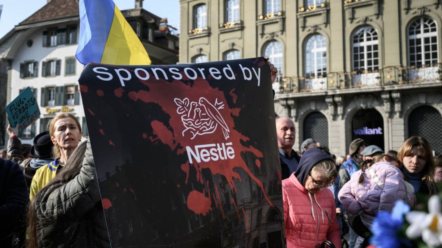 Protestujący trzymają transparent przeciwko szwajcarskiemu gigantowi spożywczemu Nestlé podczas demonstracji przeciwko rosyjskiej inwazji na Ukrainę pod Szwajcarską Izbą Parlamentu, 19.03.22.