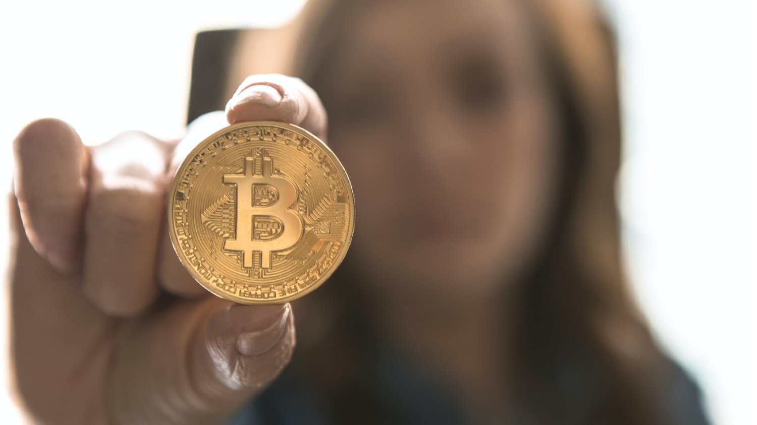 Kobieta trzyma w wyciągniętej dłoni monetę z kryptowalutą bitcoin